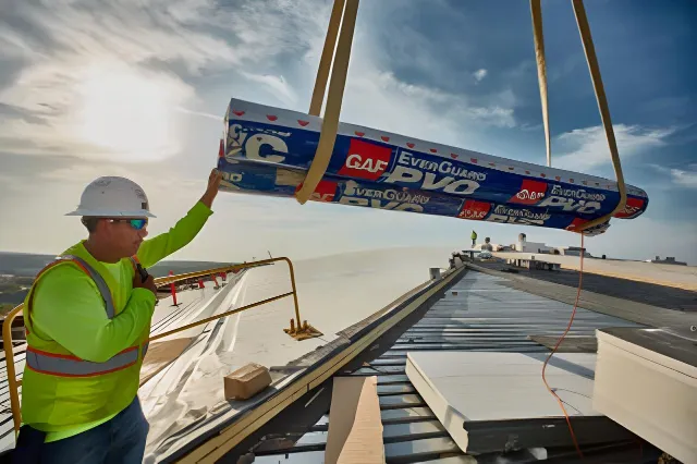 Roofer guiding a crane-lifted bundle of GAF EverGuard PVC membrane onto a commercial roof